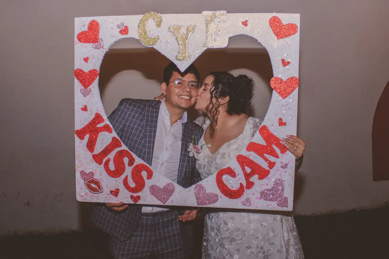 La pareja de novios sosteniendo un cartel de Kiss Cam